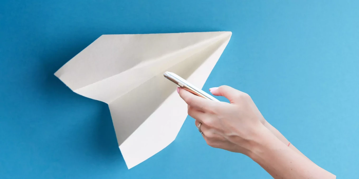avión de papel y una mano sosteniendo un celular