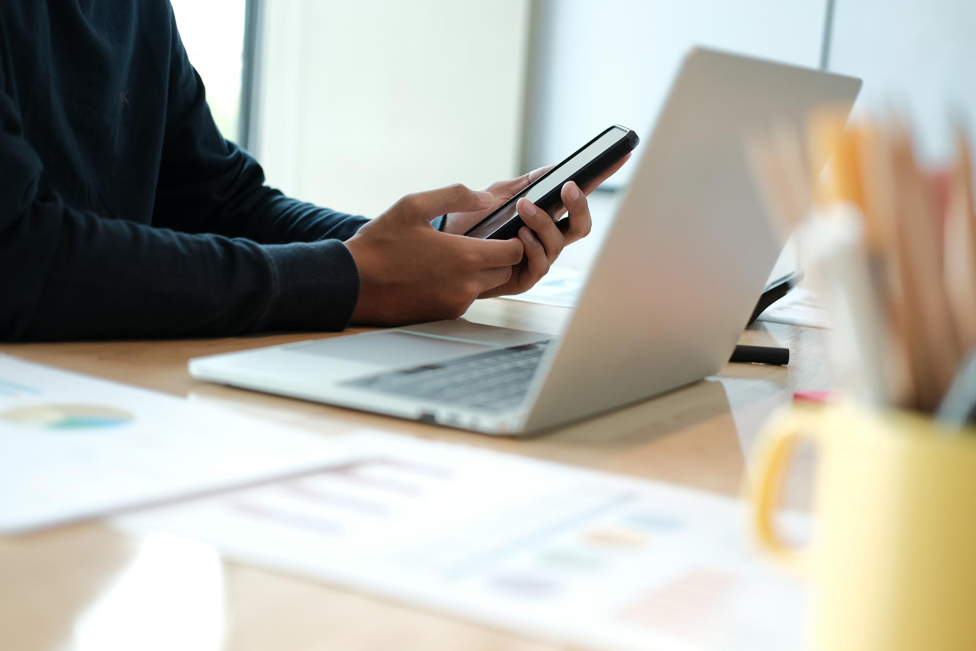 Profesional usando smartphone para gestionar conversaciones de ventas por WhatsApp en la oficina
